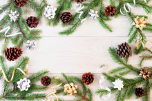 On a light wooden background in a circle frame made of fir branches, gold and silver ribbons and cones. Copy space.