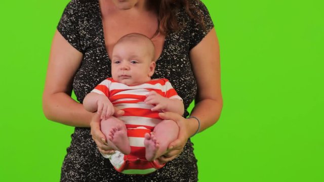 A beautiful young mom holds her newborn baby boy like and relaxes him over a green screen.