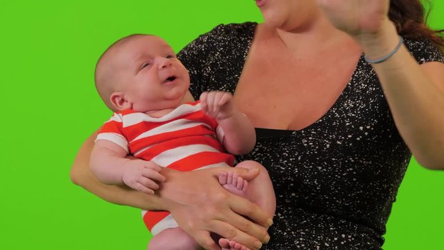 A beautiful young mom holds her newborn baby boy like Buddha and relaxes him over a green screen.