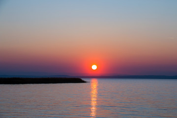 Golden setting sun over the sea just above horizon with optic straight line of light reflection on water surface, awesome natural sunset seascape with colourful sky