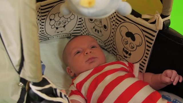A cute Newborn baby boy moves in his stroller happily over a green screen.