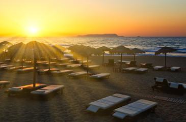 sun setting in the sea on the horizon shines through rays of sun beds and umbrellas on the sandy beach of Europe, Crete