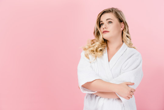 beautiful young oversize woman in bathrobe standing with crossed arms and looking away isolated on pink
