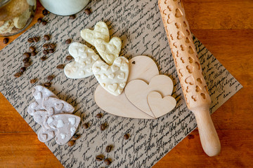 Rolling pin with a pattern on a wooden decorated table covered with baked flour. Rolled dough with a pattern and cookie in the form of a heart. Love theme. Biscuit cooking background, close-up