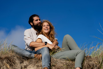 Young couple sitting on a dune in summer, relaxing