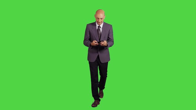 Businessman walking towards camera, using an app or texting, wearing a suit. full frontal shot over a green screen.
