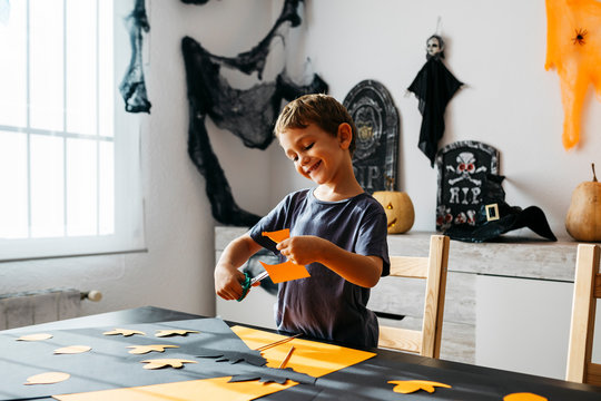 Smiling little boy cutting out for Halloween decoration at home