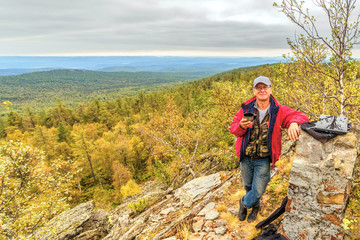 A mature tourist man stands on top of a rocky mountain.
