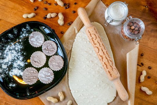 Rolling pin with a mustache pattern on a wooden decorated table covered with baked flour. Rolled dough with a pattern and cookie of various shapes. Biscuit cooking background, top view