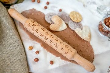 Rolling pin with a dog paw pattern on a wooden decorated table covered with baked flour. Rolled dough with a pattern and cookie of various shapes. Biscuit cooking background, top view
