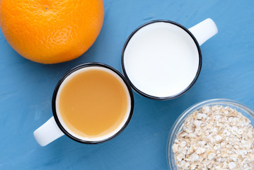 Milk and orange juice in the pretty small cups, an orange and oat flakes.