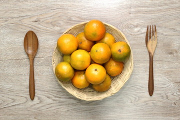 Orange in a basket and with a spoon, a wooden fork. Placed side by side and beautiful wooden background.