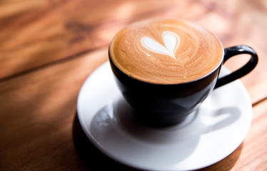 Cappuccino cup with heart latte art on wooden table background.