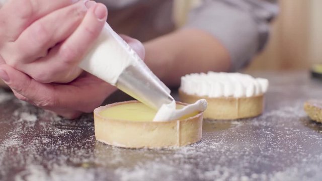 Close up hands of a confectioner decorating tartlets with swiss meringue