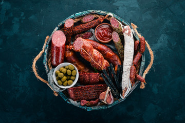 Assortment of sausages and snacks in a wooden box. Sausage Fuet, salami, paperoni. On a black...