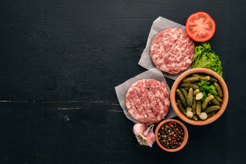 Preparation of burger. Meat, fresh vegetables, tomatoes, onions. On a black wooden background. Top view. Free copy space.