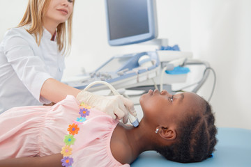 Obraz na płótnie Canvas Afro child lying when doctor scanning her neck.