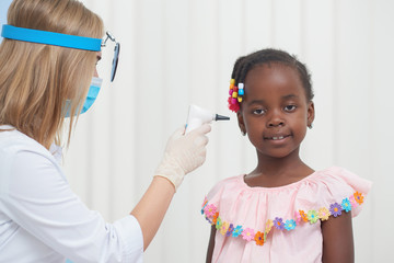 Female doctor auscultating ear of little African child.