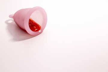 Pink isolated menstrual cup with leaked smashed tomato juice lies on a pink background.