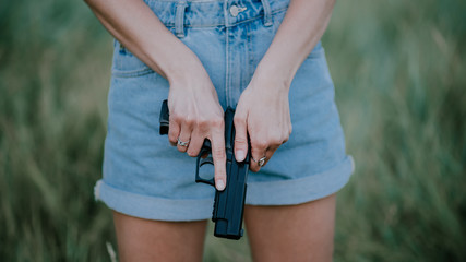 girl in denim shorts and with a gun in his hand posing in the field. Close up