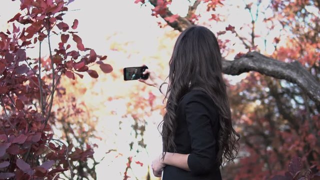 Beautiful young Caucasian girl with makeup takes selfie in autumn forest.