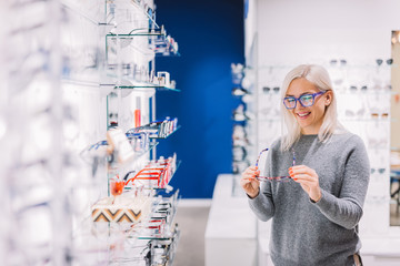 Woman looking at glasses at optic store. - obrazy, fototapety, plakaty