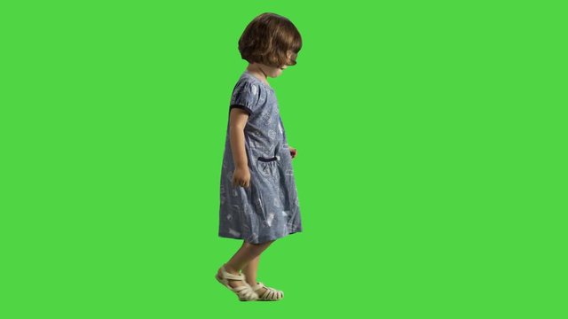 Little girl walking sideways over a green screen, happy and cheerful, spreading hands and laugh, wearing a dress.