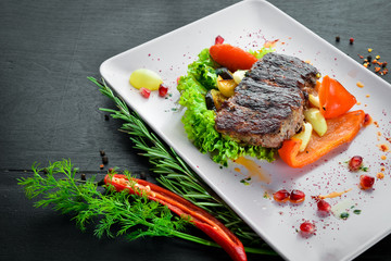 Veal steak on a plate of vegetables. On a wooden background. Top view. Free space for your text.