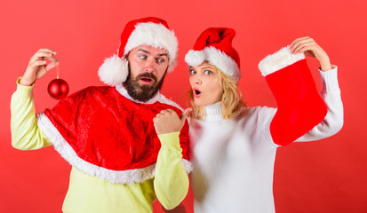 Christmas stocking tradition. Christmas celebration concept. Woman and bearded man in santa hat waiting christmas red background. Couple christmas santa costume hold sock and ornament ball