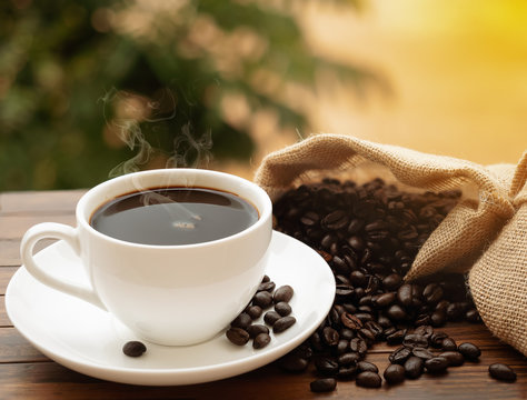 Morning hot coffee cup and coffee beans roating on the wood table