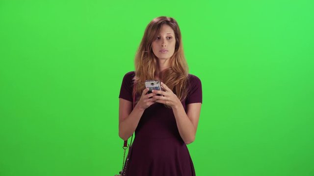 Young woman walking in a medium frontal shot over a green screen, long texting, wearing a dress, casual clothing.