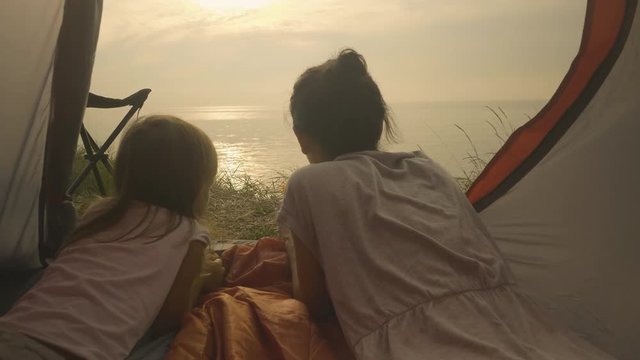 Mother and daughter laying in a tent, looking at the sea, filmed from the inside of the tent 
