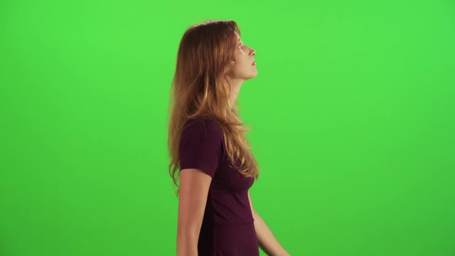A young woman walking in a medium side shot over a green screen, looking around, casual look, wearing a dress. Use for skyscrapers urban scenario.