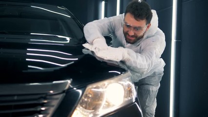Enthusiastic serviceman is cleaning a car with a cloth