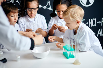 Curious adorable lovely kids studying chemical processes at elementary school, working on a group...