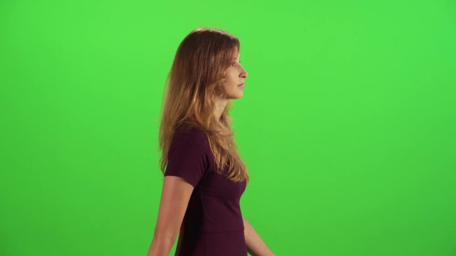 Young woman walking fast in a medium sideways shot over a green screen, bumps into people, upset.