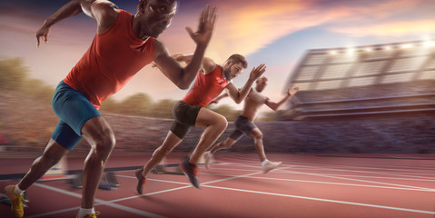 Male athletes sprinting. Three men in sport clothes run at the running track in professional stadium - obrazy, fototapety, plakaty