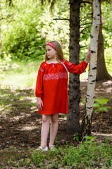 Blond young girl posing in a red dress near birch trees
