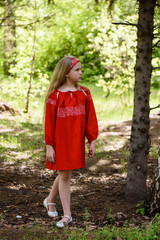 Blond young girl posing in a red dress near birch trees