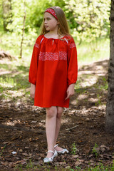 Blond young girl posing in a red dress near birch trees