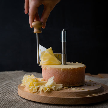 Composition of cheese tete de moine and wooden girolle (la girolle) with hand on a dark background