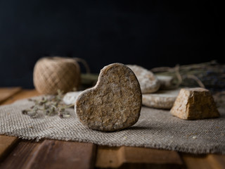 Goat cheese in the shape of a heart on the rough fabric with a sprig of lavender on a dark background