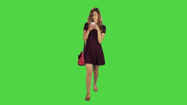 A young woman walking towards camera, texting gladly in a full body shot over a green screen.
