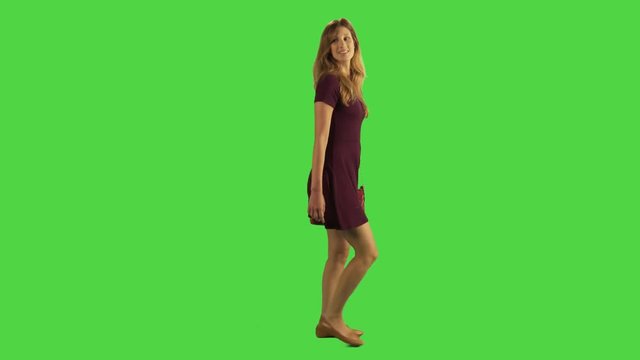 A young woman walking sideways and looking around in a full body shot over a green screen.