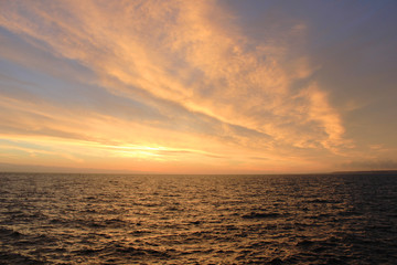 Fototapeta premium Sky Nature View of Sunset Over Calm Sea Water with Vibrant Orange Cloudscape. Beautiful Sky Background at Sunset or Sunrise, Dusk and Dawn Panoramic Skyline View with Still Water on Summer Season Day