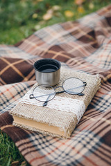Book, glasses and hot tea from a thermos lie on a blanket