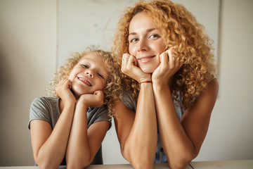 Happy loving family. Mother and daughter with curly blonde hair looking at camera, smiling and...