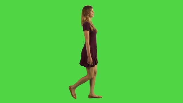 Young woman walking sideways while looking upwards in full body shot over a green screen.