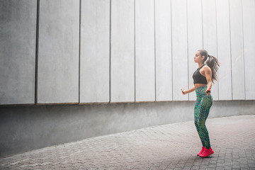 Wel-shaped young woman jumping with rope alone in corridor. She exercises very hard. Model has...