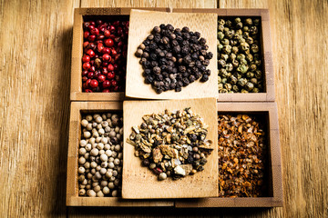 spices for a tasty meal on an old wooden table: red pepper, green pepper, black pepper, white pepper, ground chili, mixture of spices, salt
